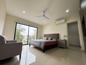 A bedroom with a bed, a chair, a desk, a ceiling fan, and a large window.