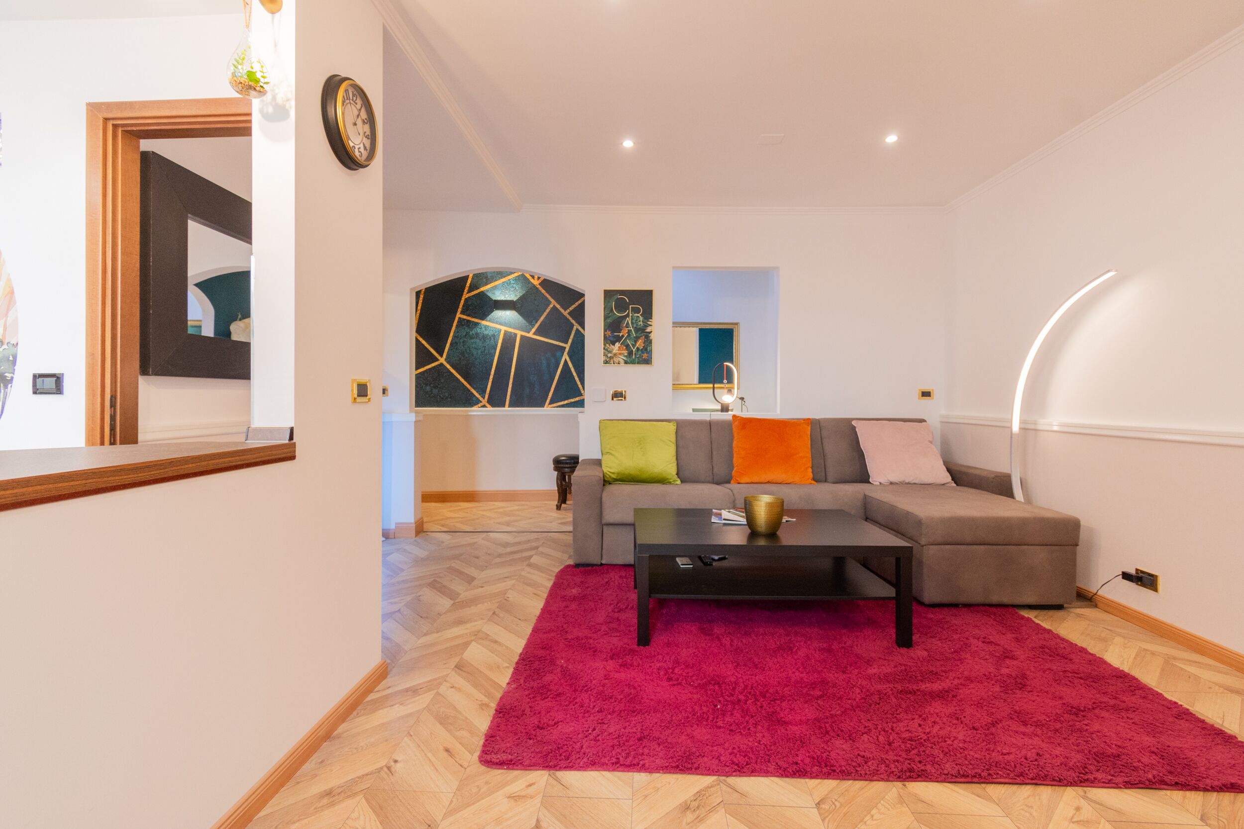 En moderne stue med sofa, sofabord og et farverigt rødt gulvtæppe.
