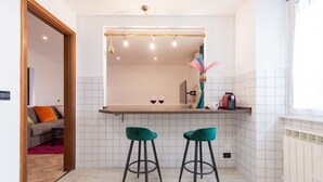 A modern kitchen with white tiles, two green bar stools, and a wooden countertop.
