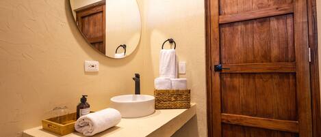 A bathroom with a round mirror, a white sink, a wooden door, and a towel rack with towels.