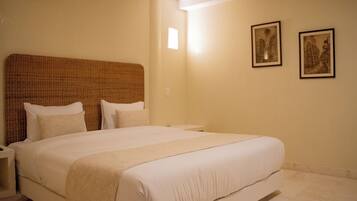 A neatly made bed with a headboard, a bedside table, and two framed pictures on the wall.