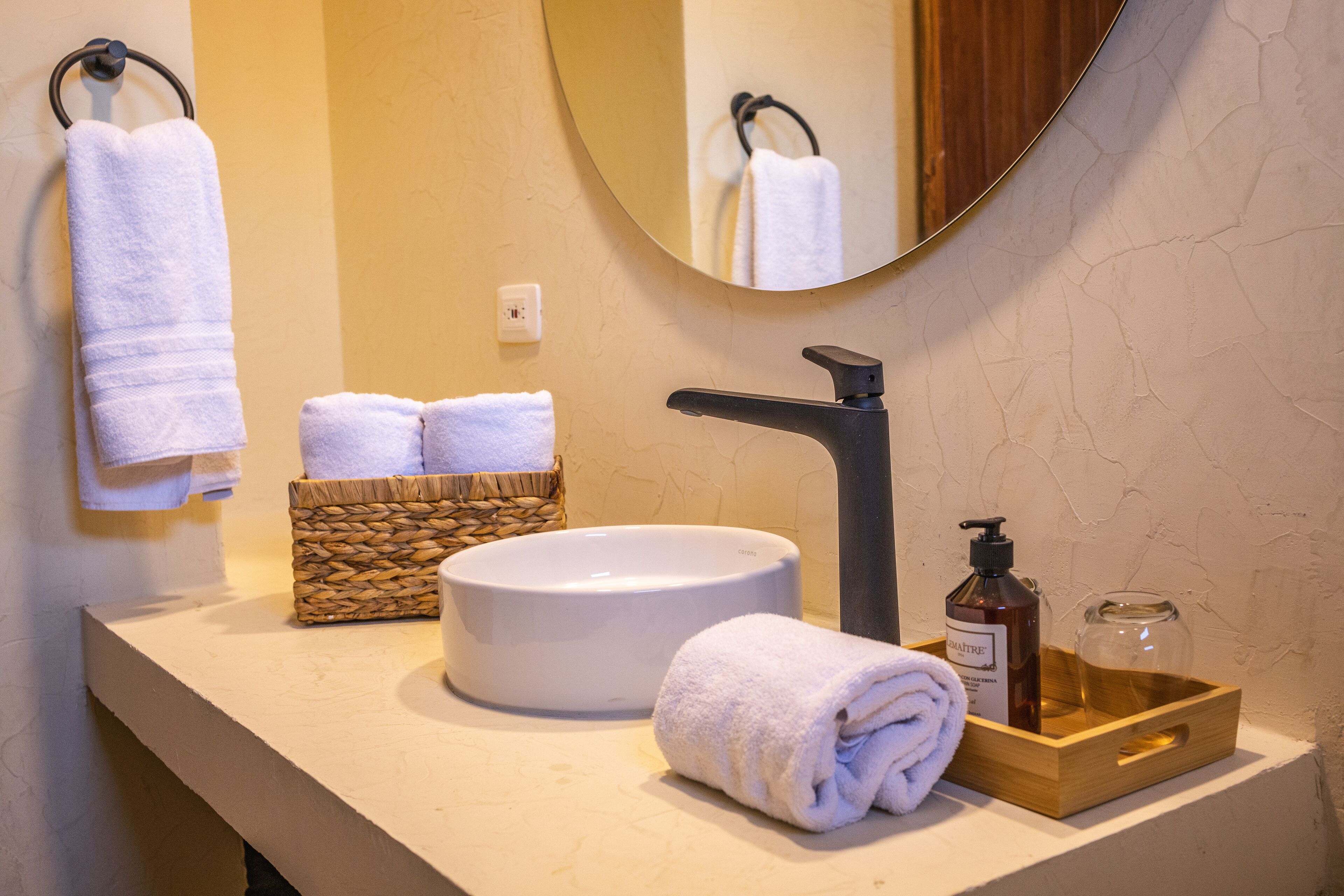 A bathroom with a round sink, a mirror, and a wooden tray with toiletries.