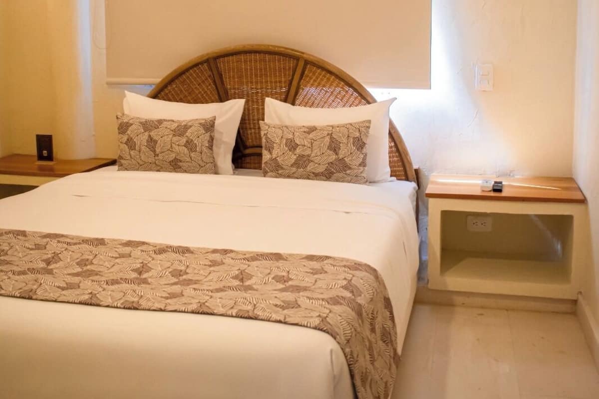 Una cama bien hecha con una colcha estampada, un cabecero de mimbre y dos mesitas de noche con lámparas.