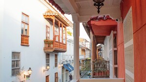A balcony with a wooden table and chairs, overlooking a street with buildings and a hanging lantern.