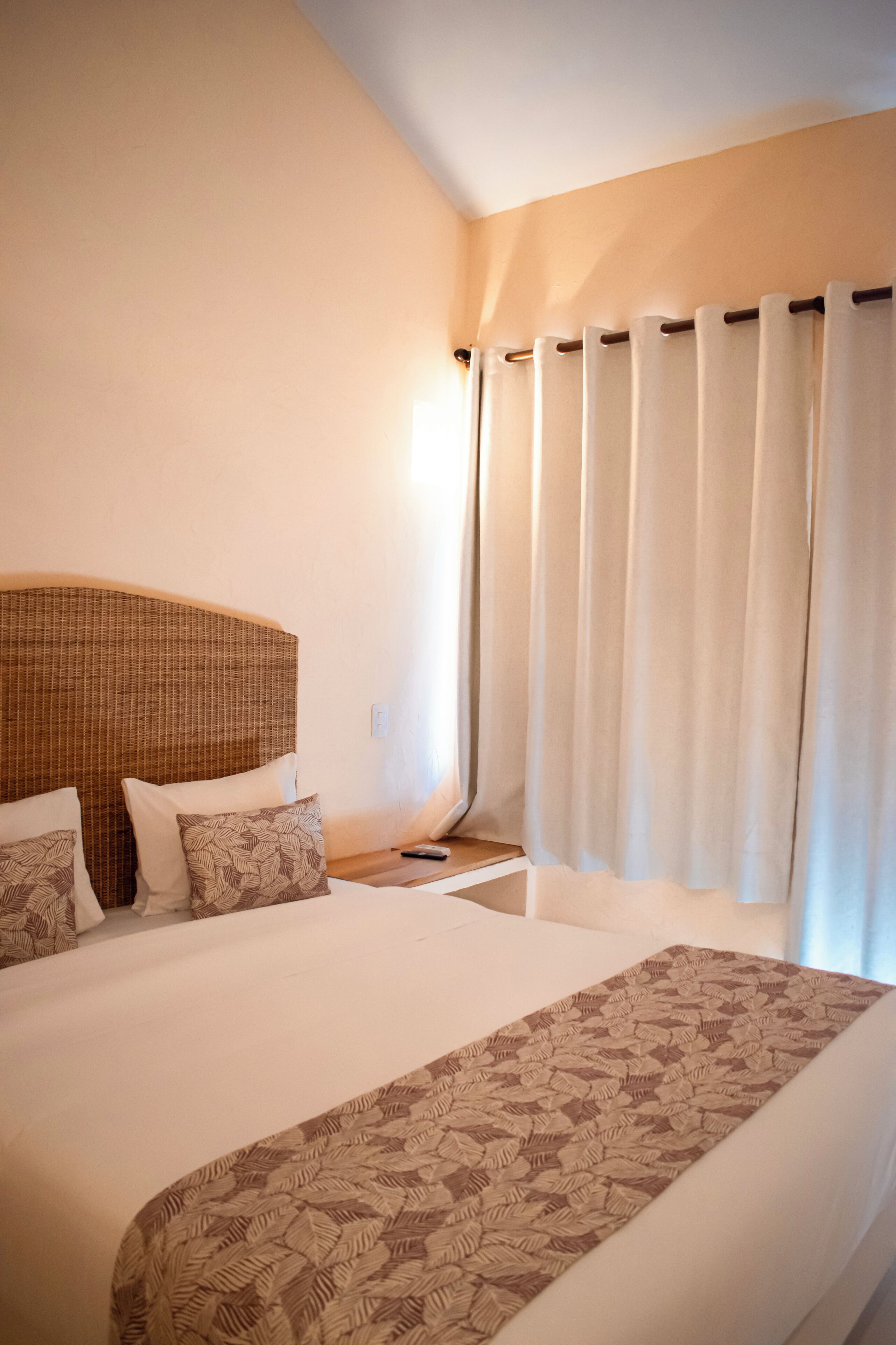 A hotel room with a large bed, a wooden headboard, a bedside table, and a window with curtains.