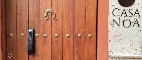 A wooden door with brass handles and a keyhole, a brass door knocker, and a sign reading "CASA NOA".
