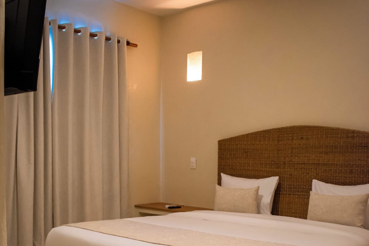 Habitación de hotel con una cama grande, un televisor de pantalla plana en la pared y una mesita de noche pequeña.