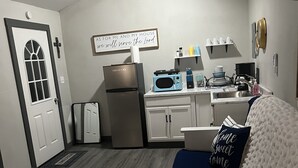 Un espacio habitable compacto con kitchenette, una cama con almohadones decorativos y un baño pequeño.