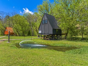 A rustic cabin with a metal roof, elevated on stilts, surrounded by lush greenery and a small pond. - Treehouse A-Frame on Goat farm (Newport)