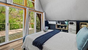 Ein Schlafzimmer mit einem großen Bett, Blick ins Freie und einer Küchenzeile mit Grundausstattung.