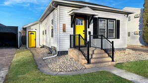 A single-story house with a yellow front door, a black front porch, and a garage. - The Bunga Glow: Modern, Cozy & Bright Near Downtown (Sioux Falls)