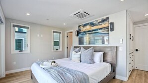 Ein Schlafzimmer mit einem großen Bett, einem Bild darüber und einer Tür mit Griff rechts.
