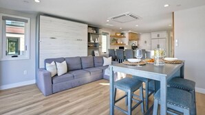 Eine moderne Küche mit Essbereich, ausgestattet mit einem grauen Sofa, blauen Barhocker und einer Kücheninsel mit einer Karaffe und Gläsern.