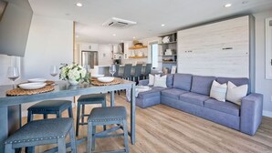 A modern kitchen with a dining area, a gray sofa, and a large whiteboard on the wall.