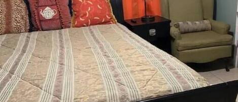 A bedroom with a bed, a nightstand, a chair, and an orange curtain.