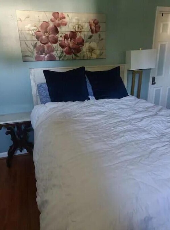 A bedroom with a bed, pillows, a nightstand, a lamp, and a floral artwork on the wall.