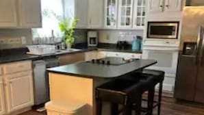 A kitchen with wooden flooring, white cabinetry, a central island with bar stools, a microwave, and a refrigerator.