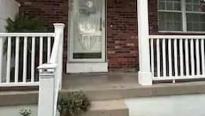 A two-story house with a brick facade, a front door, and a small porch with white railings.