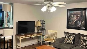 A living room with a television, a desk, a chair, a sofa, and a coffee table.