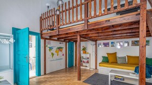 Una camera mansardata con soffitto in legno, un letto a castello, una mappa del mondo appesa al muro, un divano con cuscini e una libreria.