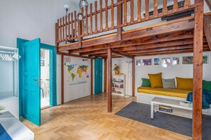 A loft-style room with a wooden ceiling, a bunk bed, a world map on the wall, a sofa with cushions, and a bookshelf.