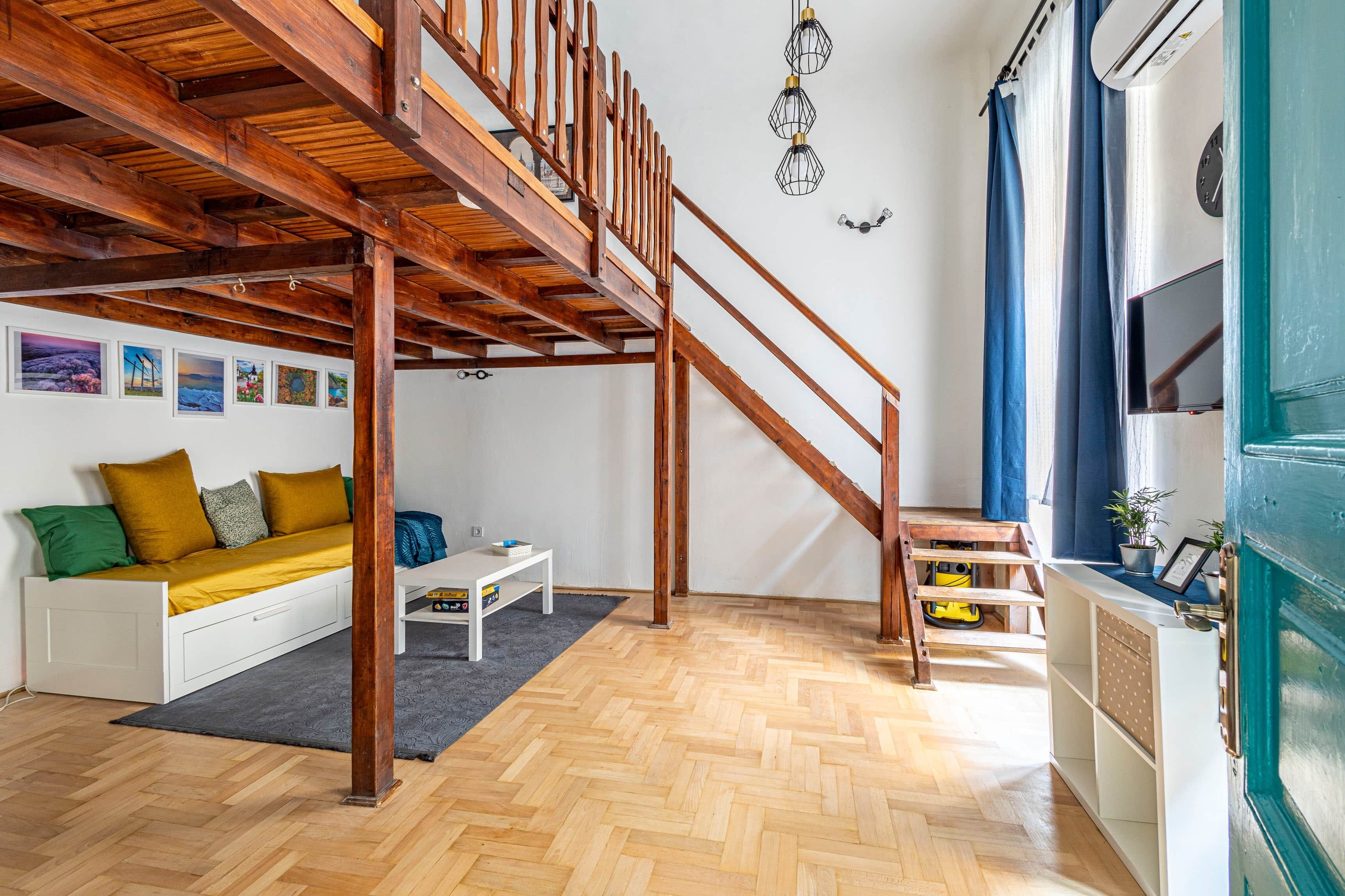 A multi-level living space with a wooden staircase, a sofa with cushions, a small table, and a herringbone-patterned floor.