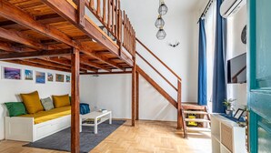 Un ambiente living su più livelli con una scala in legno, un divano con cuscini, un tavolino e un pavimento a disegno a spina di pesce.