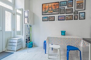 A room with a white desk, a chair, a table with a polka dot tablecloth, and a wall with framed pictures.