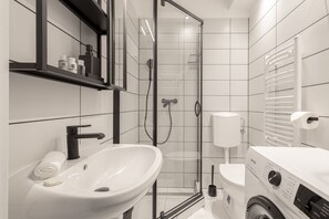 Un baño moderno con ducha acristalada, lavabo blanco, inodoro y lavadora integrada.