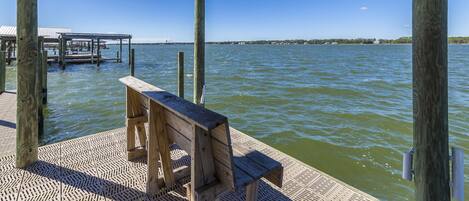 A wooden bench on a pier with a view of the water and distant shoreline.