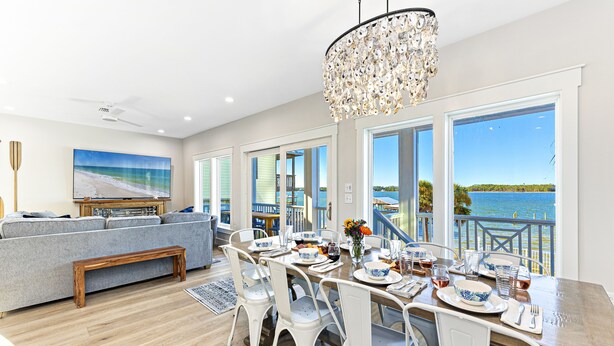 A dining area with a view of the water, a chandelier, and a large painting on the wall. - Amazing New Lagoon View Home (Gulf Shores)