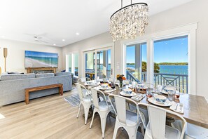A dining area with a view of the water, a chandelier, and a large painting on the wall. - Amazing New Lagoon View Home (Gulf Shores)
