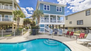 A pool area with a blue pool, lounge chairs, and a two-story building with balconies. - Amazing New Lagoon View Home (Gulf Shores)