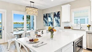 A modern kitchen with a large island, white cabinetry, and a view of the sea. - Amazing New Lagoon View Home (Gulf Shores)