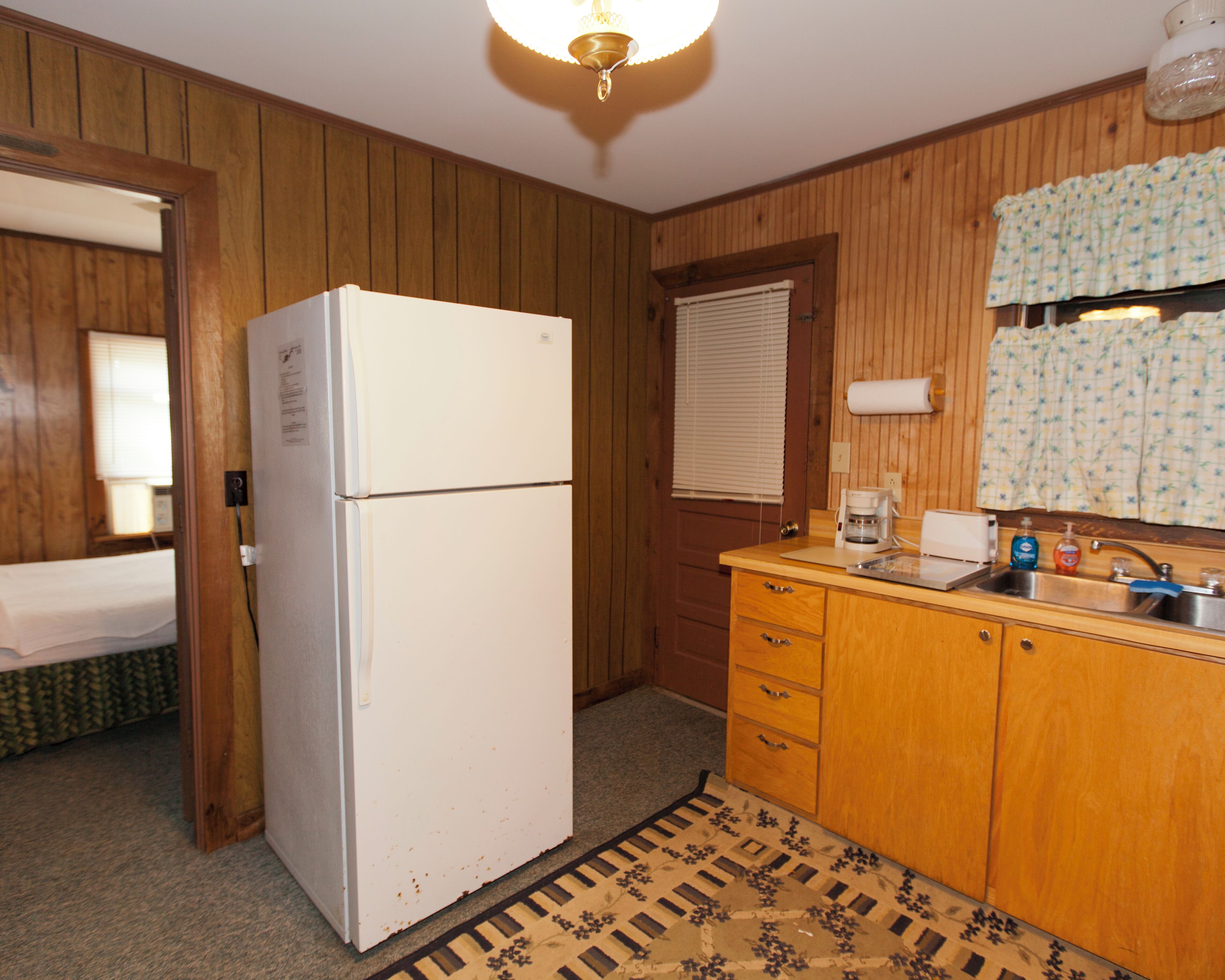 A compact kitchen with wooden paneling, a white refrigerator, a sink with a faucet, and a patterned rug.