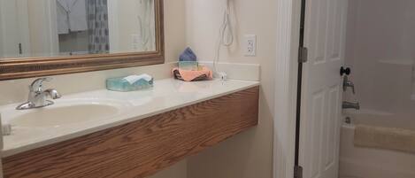 Un baño con tocador de madera, un espejo grande, un secador de pelo y zona de ducha.