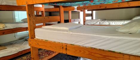 Dormitorio con literas de madera, ropa de cama blanca y una alfombra estampada.