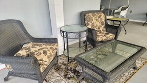 Quarto com móveis de vime, incluindo duas cadeiras e uma mesa com tampo de vidro.