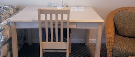 A small, neatly arranged room with a white desk, a chair, a mirror, and a wicker chair.