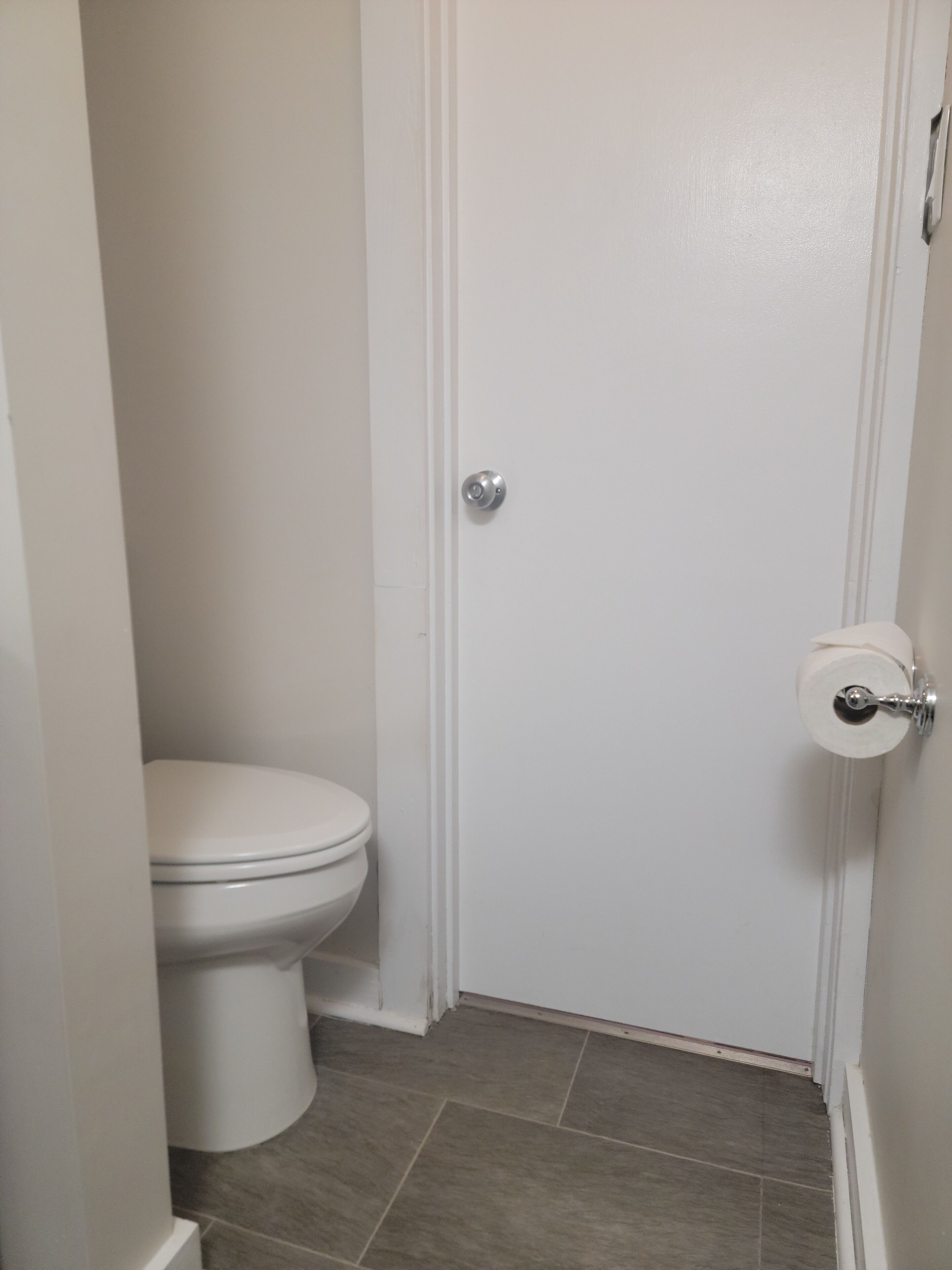 Une petite salle de bain propre, avec des toilettes blanches et une porte dotée d’un porte-rouleau de papier toilette.