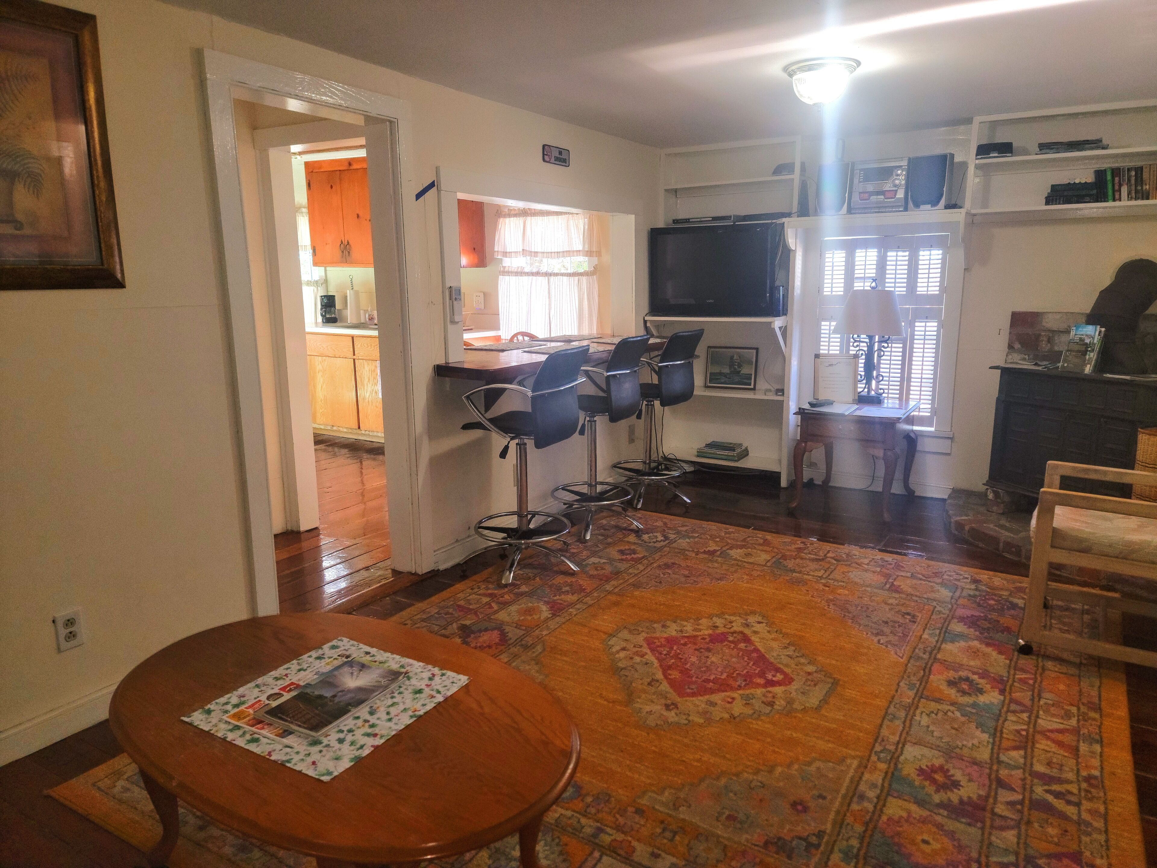 Una sala de estar acogedora con una mesa de comedor de madera, un tapete estampado y una cocina visible a través de un umbral abierto.