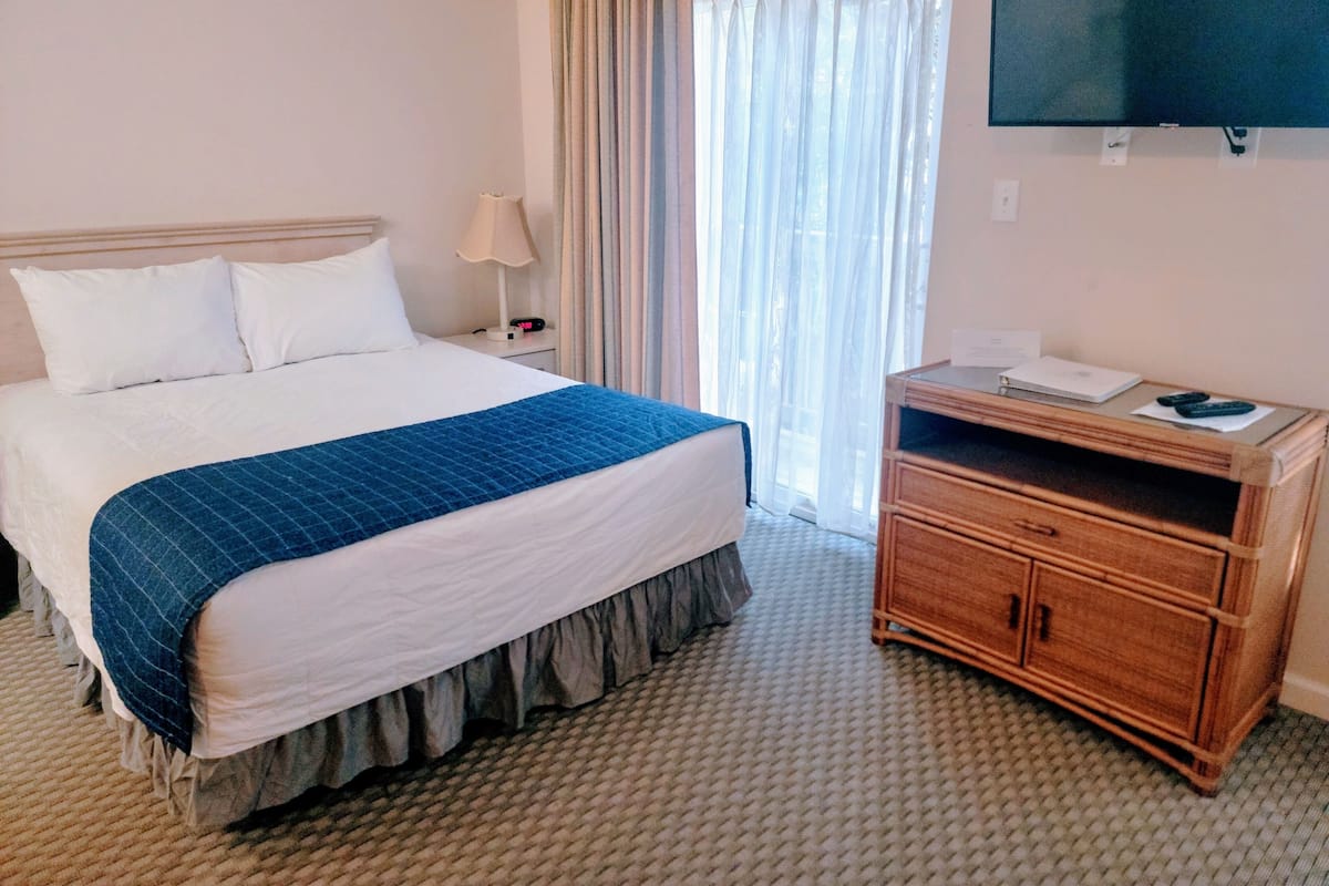 A hotel room with a bed, a nightstand, a TV, and a wooden dresser.