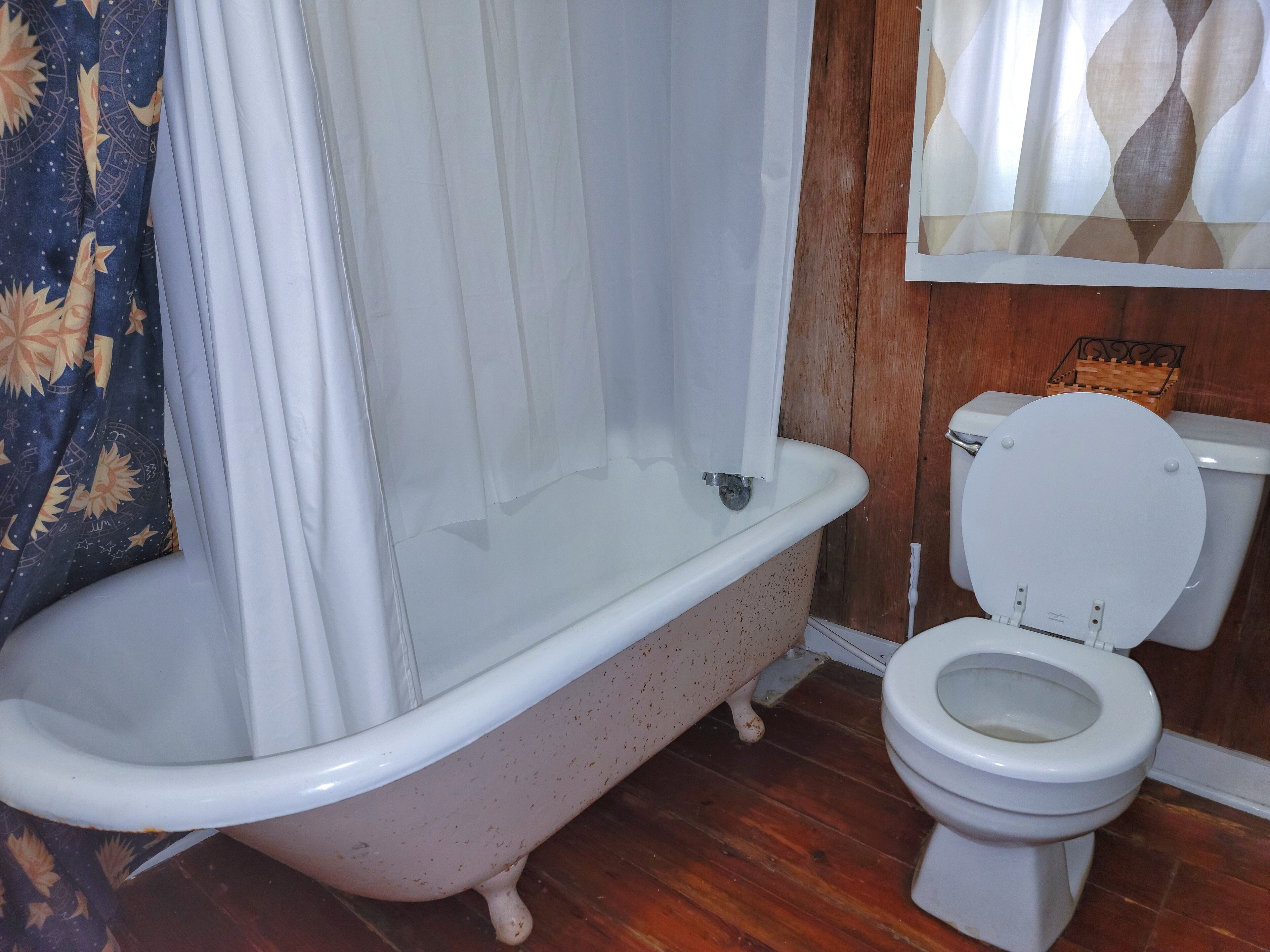 A bathroom with a freestanding bathtub, a toilet, and a wooden floor.