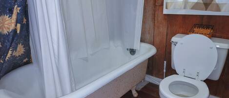 A bathroom with a freestanding bathtub, a toilet, and a wooden floor.