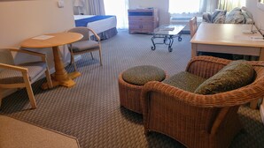 Quarto de hotel com cama, mesa de jantar, sofá, poltrona, televisão e um quadro na parede.