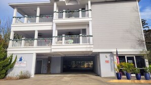 Um hotel de vários andares com área de estacionamento coberta, uma placa indicando que é um hotel e uma bandeira do lado de fora.
