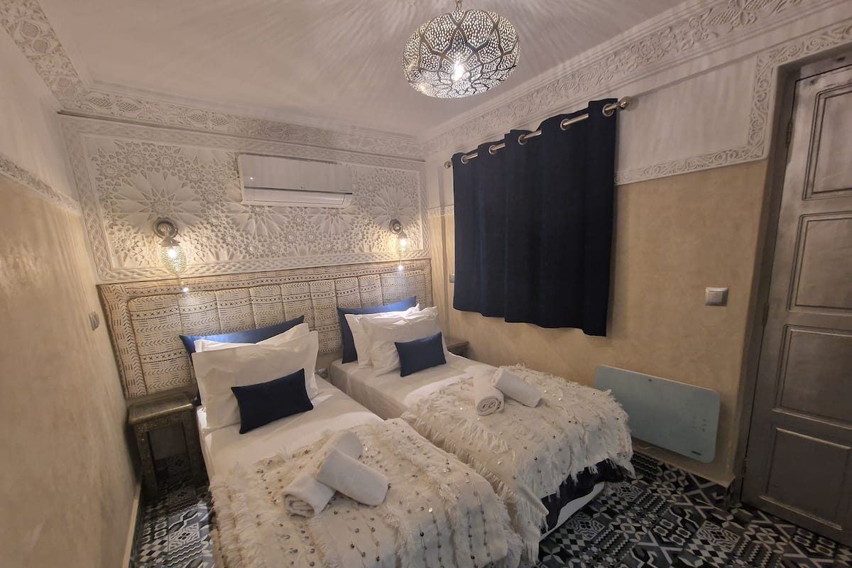 Habitación de hotel con dos camas, paredes con diseño, una lámpara decorativa en el techo y suelo estampado.