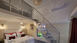A bedroom with a large bed, a staircase, and a view of a colorful outdoor area. - Riad Explore (Marrakech)