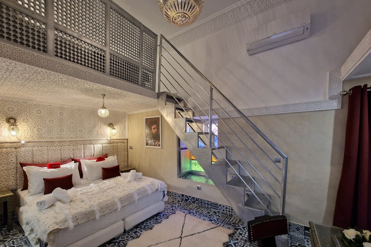 Un dormitorio con una cama grande, una escalera y vistas a un espacio exterior colorido.