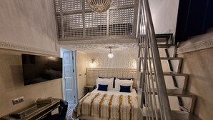 A hotel room with a bed, a desk, a chair, a TV, and a staircase. - Riad Explore (Marrakech)